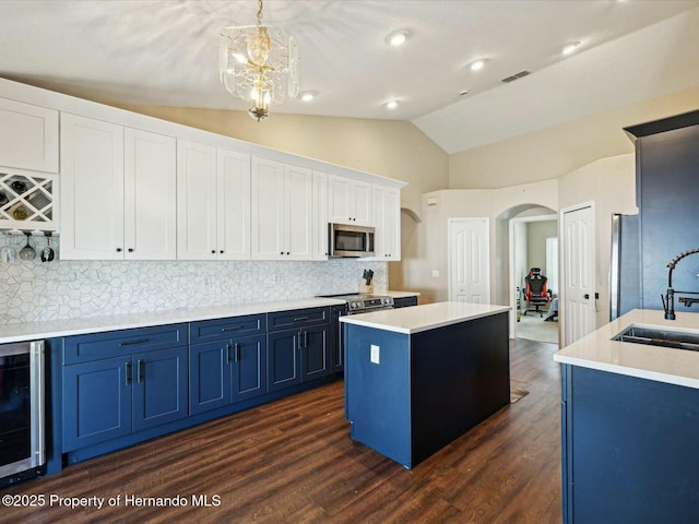 kitchen featuring stainless steel microwave, a sink, blue cabinetry, arched walkways, and beverage cooler