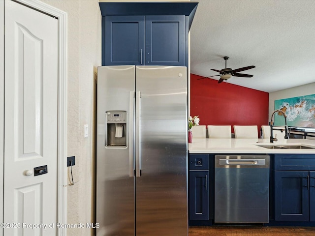 kitchen with a sink, stainless steel appliances, blue cabinetry, a ceiling fan, and vaulted ceiling