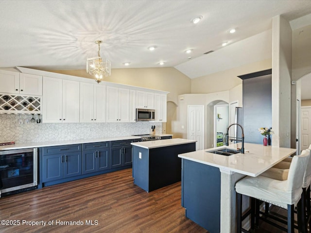 kitchen featuring a sink, wine cooler, blue cabinetry, arched walkways, and appliances with stainless steel finishes