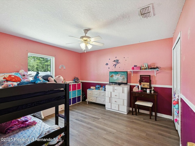bedroom featuring a textured ceiling, visible vents, ceiling fan, and wood finished floors