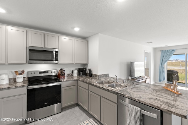 kitchen featuring a sink, gray cabinets, stone counters, a peninsula, and appliances with stainless steel finishes