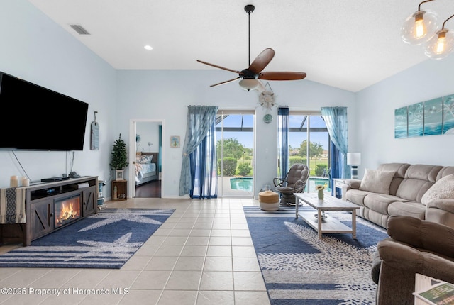 living room with visible vents, a glass covered fireplace, a ceiling fan, light tile patterned floors, and vaulted ceiling