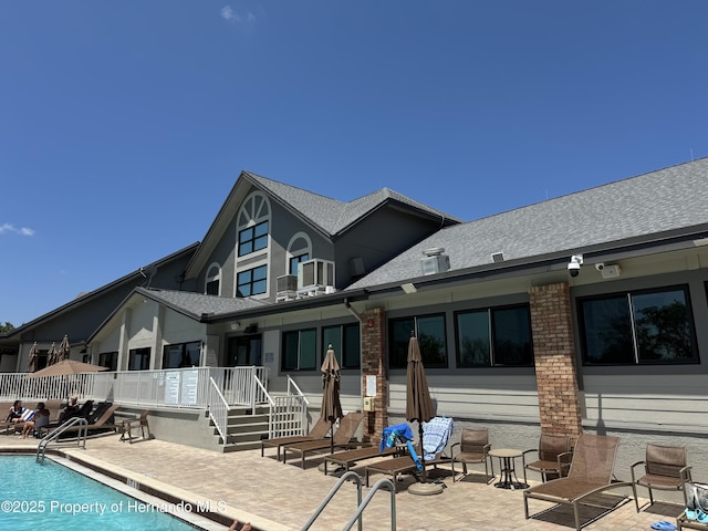 back of house with a shingled roof, a community pool, and a patio area