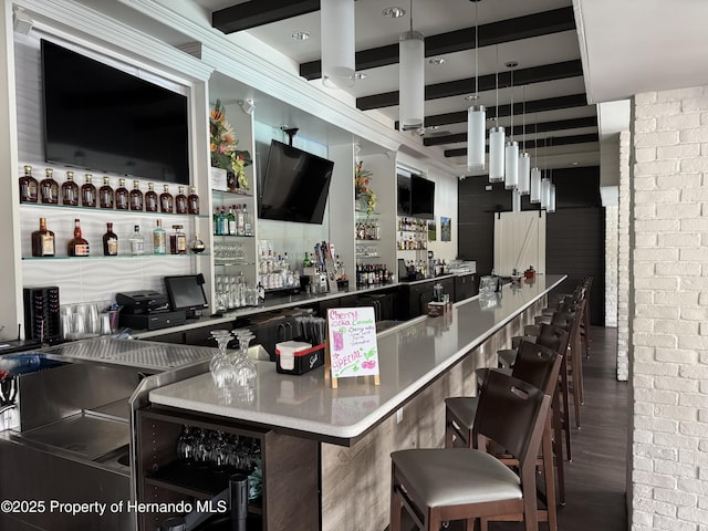 bar with indoor wet bar, wood finished floors, brick wall, and beamed ceiling