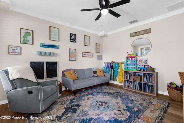living room featuring a ceiling fan, visible vents, wood finished floors, baseboards, and ornamental molding