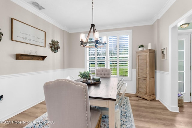 dining space with visible vents, ornamental molding, light wood finished floors, and a chandelier