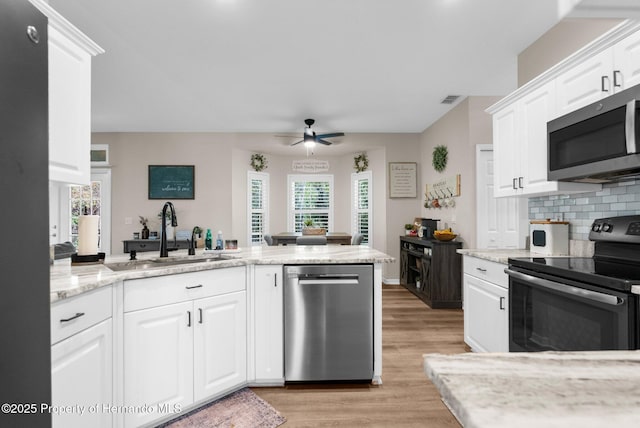 kitchen featuring appliances with stainless steel finishes, a sink, light wood finished floors, backsplash, and visible vents
