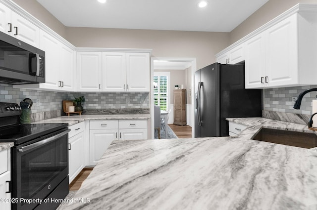 kitchen featuring light stone counters, a sink, white cabinetry, and black appliances