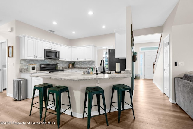 kitchen featuring freestanding refrigerator, a breakfast bar, stainless steel microwave, white cabinets, and electric stove