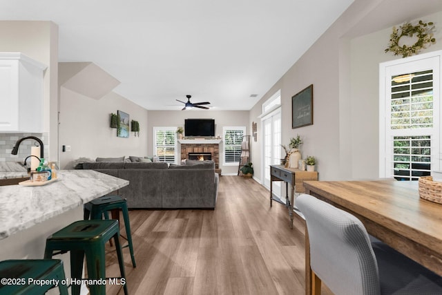 living room with a ceiling fan, light wood finished floors, and a lit fireplace