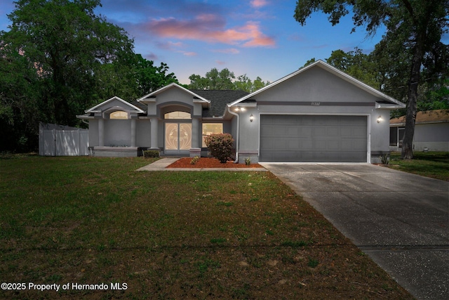 ranch-style home with driveway, a lawn, fence, an attached garage, and stucco siding