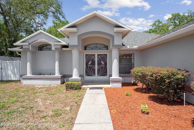 doorway to property featuring roof with shingles, stucco siding, and fence
