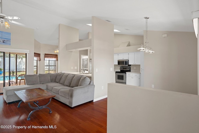 living area featuring baseboards, dark wood-style flooring, ceiling fan with notable chandelier, and high vaulted ceiling