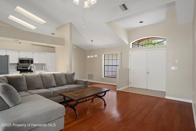living room with visible vents, ceiling fan with notable chandelier, wood finished floors, and high vaulted ceiling