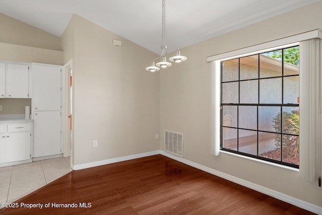 unfurnished dining area featuring visible vents, vaulted ceiling, baseboards, a chandelier, and light wood-style flooring