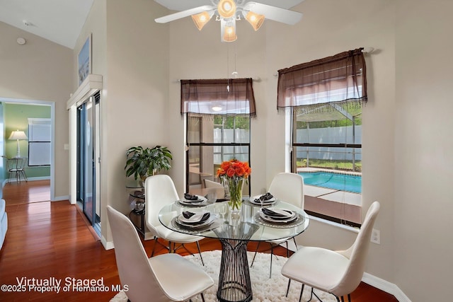dining area featuring baseboards, a ceiling fan, wood finished floors, and a towering ceiling
