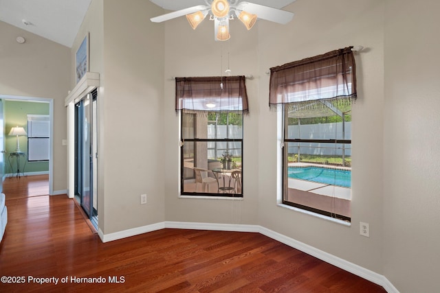 spare room with baseboards, a ceiling fan, wood finished floors, and a towering ceiling