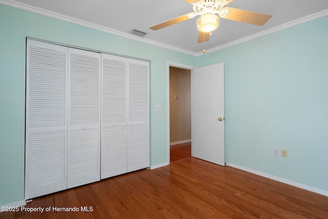 unfurnished bedroom with visible vents, wood finished floors, baseboards, a closet, and ornamental molding