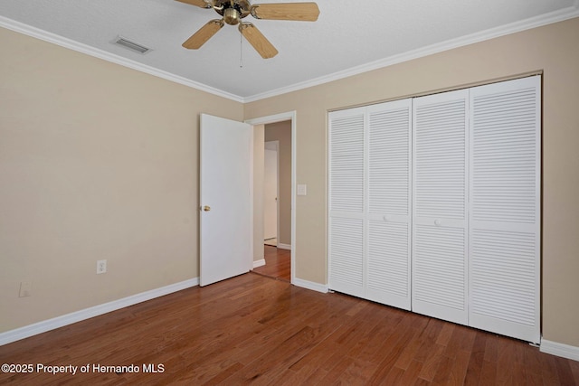 unfurnished bedroom with visible vents, ornamental molding, a closet, wood finished floors, and baseboards