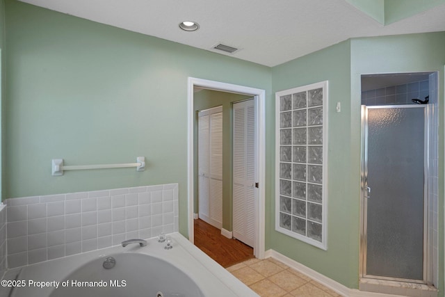 bathroom featuring tile patterned flooring, baseboards, a tub with jets, visible vents, and a stall shower