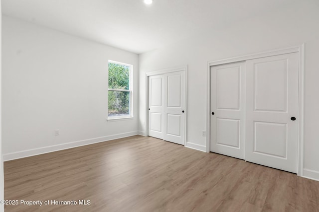 14042 Amero Ln, Spring Hill, FL 34609 - unfurnished bedroom with baseboards, multiple closets, and wood finished floors