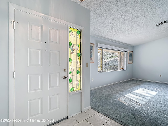 entryway with light colored carpet, a textured ceiling, light tile patterned floors, and visible vents