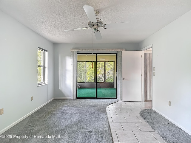 tiled empty room with a textured ceiling, ceiling fan, and baseboards