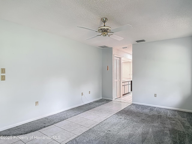 carpeted spare room featuring visible vents, a ceiling fan, a textured ceiling, and tile patterned floors