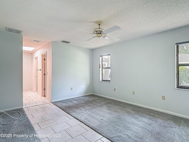spare room featuring visible vents, a ceiling fan, light tile patterned floors, and light colored carpet
