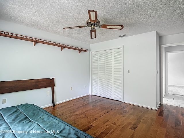 unfurnished bedroom with a textured ceiling, baseboards, wood finished floors, visible vents, and a closet