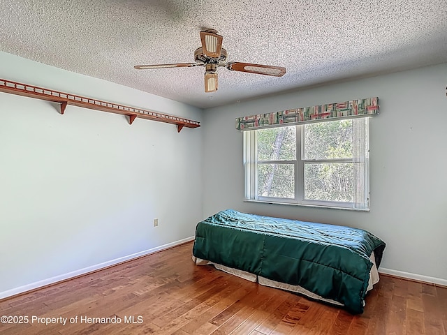 bedroom featuring ceiling fan, a textured ceiling, baseboards, and wood finished floors