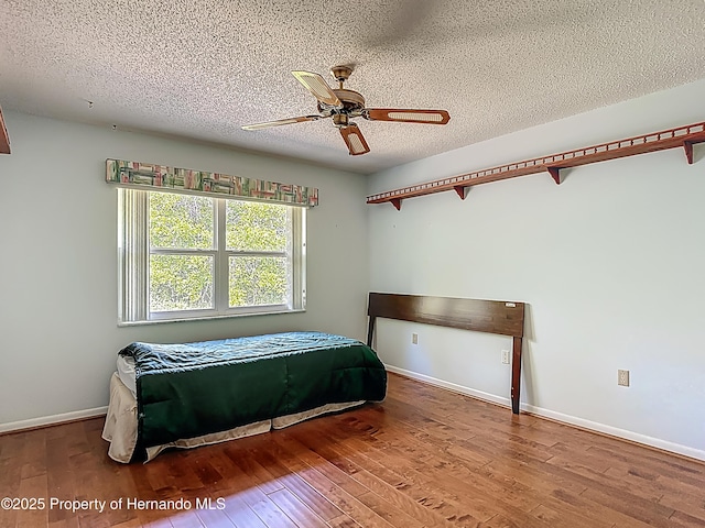 bedroom featuring baseboards, a textured ceiling, and wood finished floors