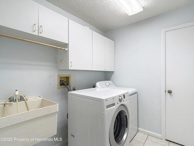 laundry area with a textured ceiling, cabinet space, light tile patterned floors, a sink, and washer and clothes dryer