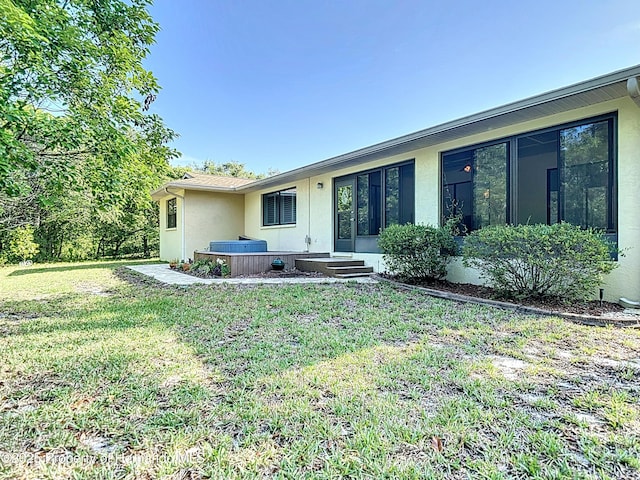 back of property featuring a hot tub, stucco siding, and a yard