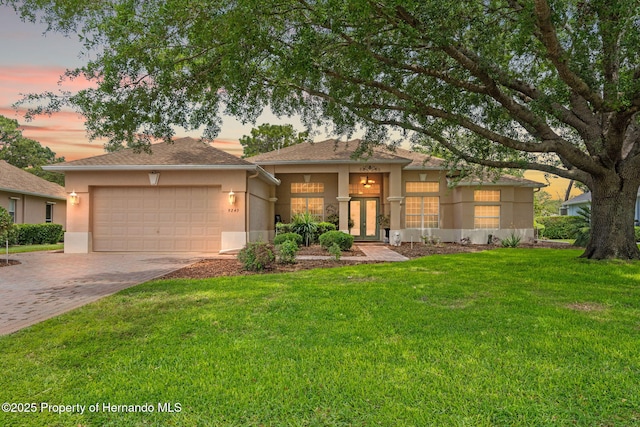 view of front facade with a front lawn, a garage, stucco siding, french doors, and driveway