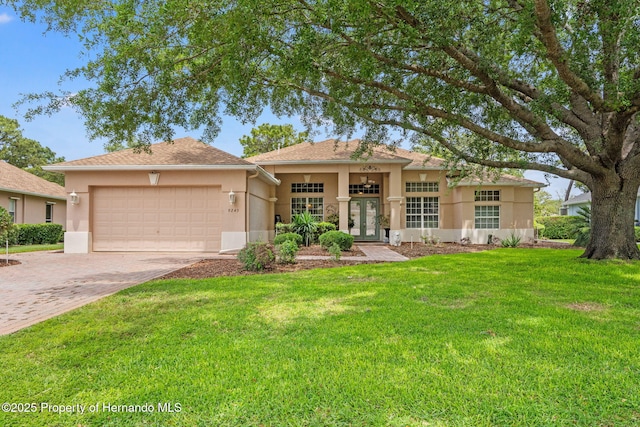 ranch-style home featuring a front lawn, stucco siding, french doors, an attached garage, and driveway
