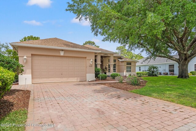 ranch-style house with a garage, stucco siding, a front lawn, and decorative driveway