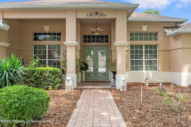 entrance to property with french doors, stucco siding, a porch, and roof with shingles