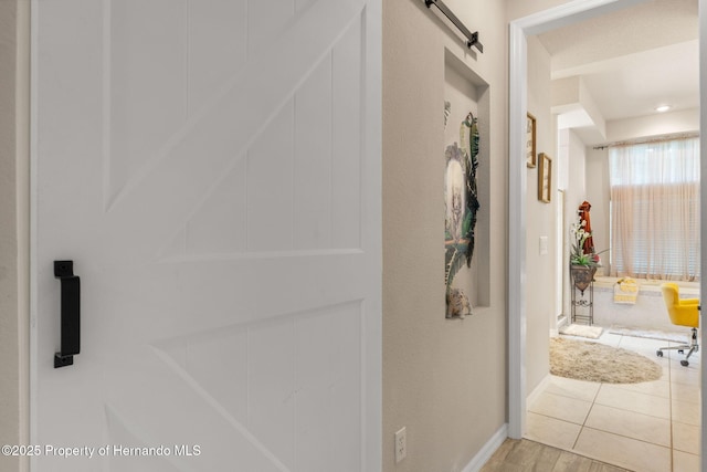 hall with baseboards, a barn door, and wood finished floors