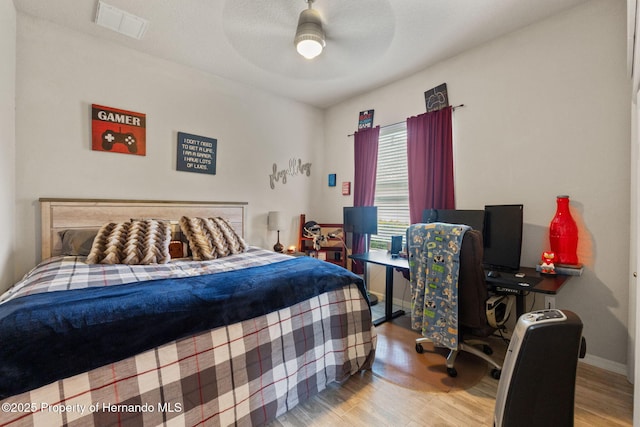 bedroom with baseboards, ceiling fan, wood finished floors, and visible vents