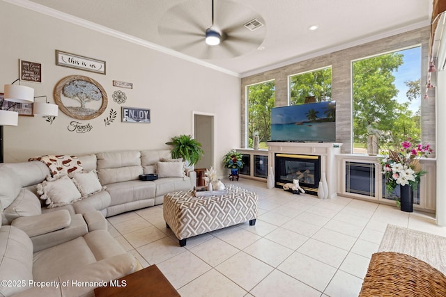 tiled living room with visible vents, ornamental molding, a glass covered fireplace, and ceiling fan