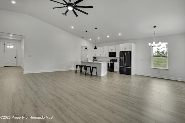 unfurnished living room with baseboards, plenty of natural light, lofted ceiling, and ceiling fan with notable chandelier