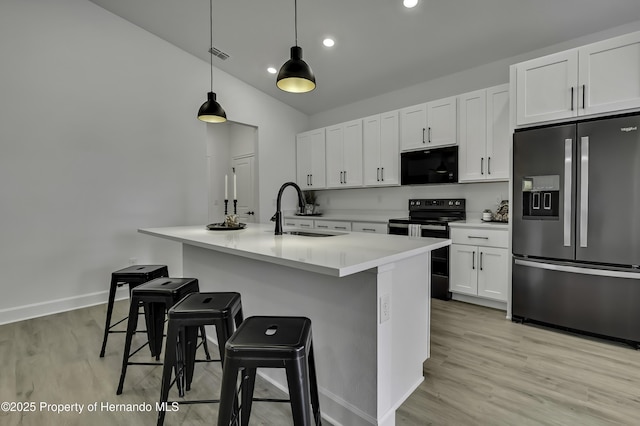 kitchen with a sink, light wood finished floors, an island with sink, white cabinetry, and black appliances