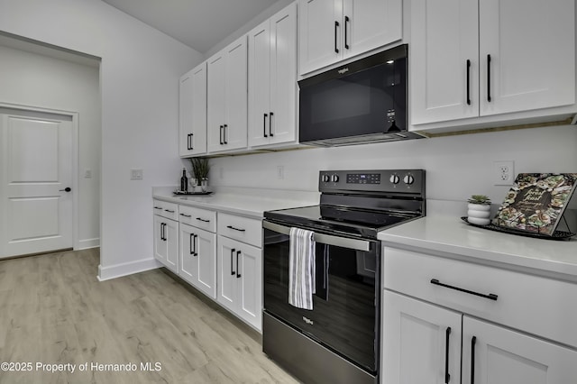 kitchen featuring electric range, black microwave, light wood-style floors, light countertops, and white cabinetry