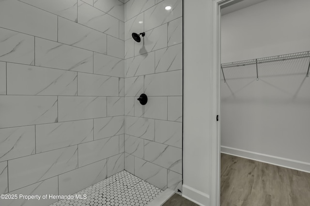 full bath featuring baseboards, a spacious closet, tiled shower, and wood finished floors