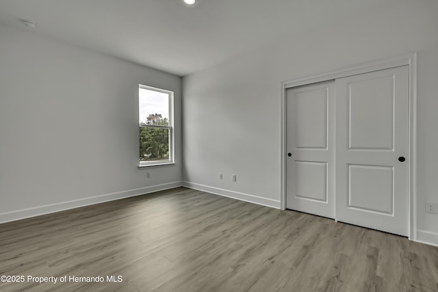 unfurnished bedroom featuring baseboards, wood finished floors, and a closet