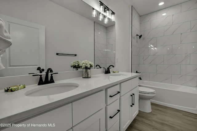full bath with a sink, double vanity, toilet, and wood finished floors