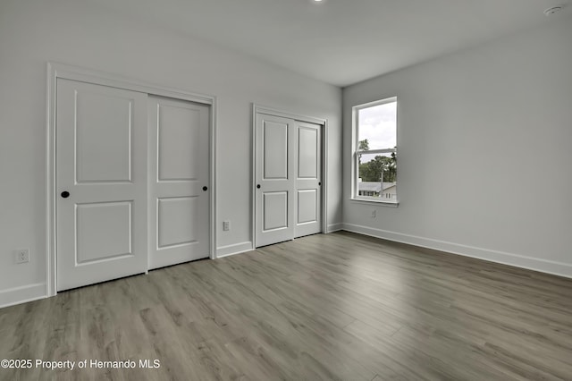 unfurnished bedroom with baseboards, multiple closets, and wood finished floors