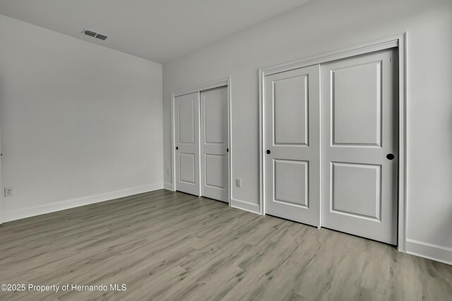 unfurnished bedroom featuring baseboards, multiple closets, wood finished floors, and visible vents