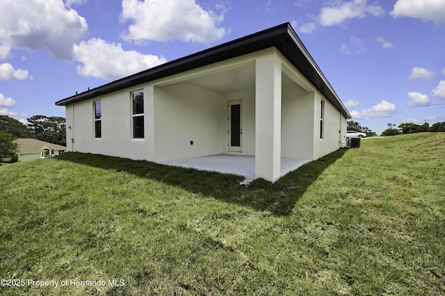 rear view of property with a lawn, central air condition unit, a patio area, and stucco siding